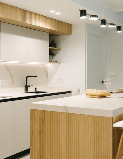 chica toma vino cocina blanca abierta al salón con palillería de Linea 3 Cocinas