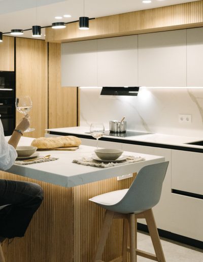 mujer toma vino en cocina blanca con palillería de Linea 3 Cocinas abierta al salón