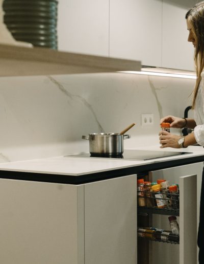 mujer cocinando en olla en vitroiceramica en cocina blanca